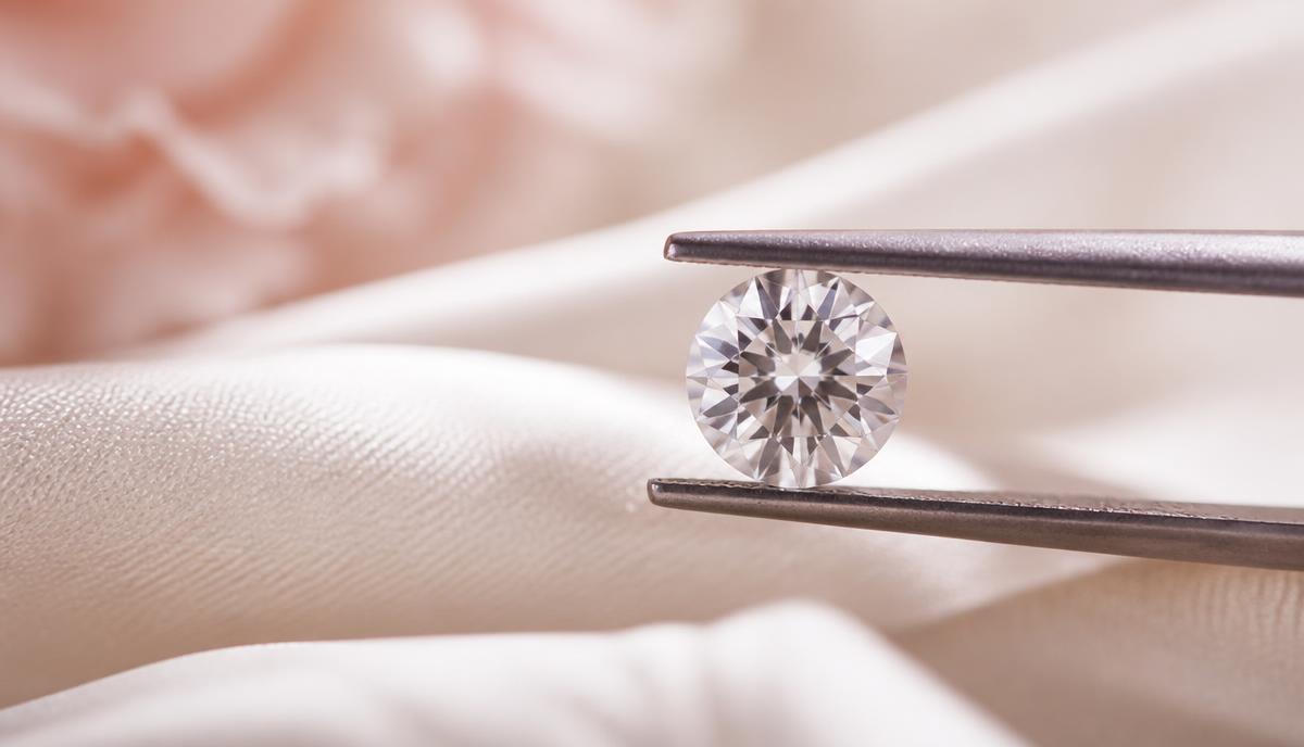 Lös briljantslipad diamant hållen i en pincett mot ljus bakgrund